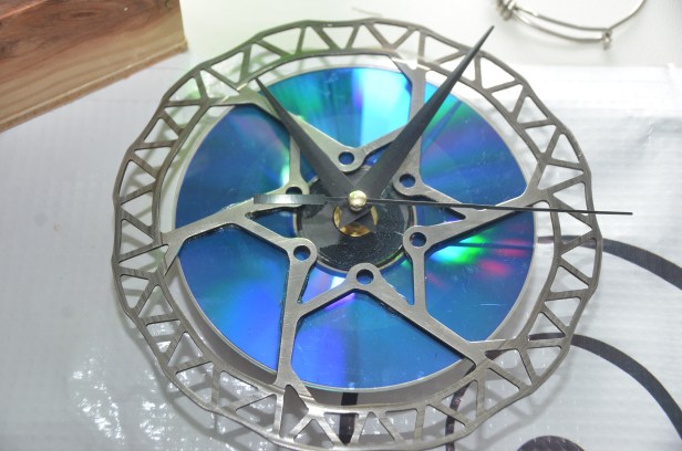 Reloj de pared artesanal hecho con un disco de freno de bicicleta y un CD, upcycling de piezas de bici por Soy Ciclista Urbano en Santo Domingo, RD.