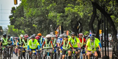 Grupo masivo de ciclistas urbanos con chalecos reflectantes amarillos en una avenida de Santo Domingo, República Dominicana.