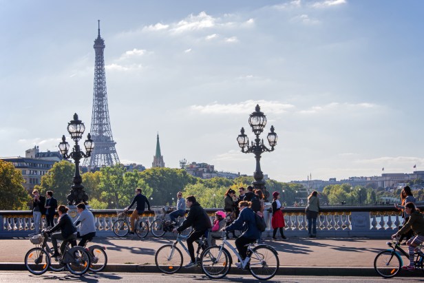 Personas circulando en bicicleta en un puente de París con la Torre Eiffel al fondo